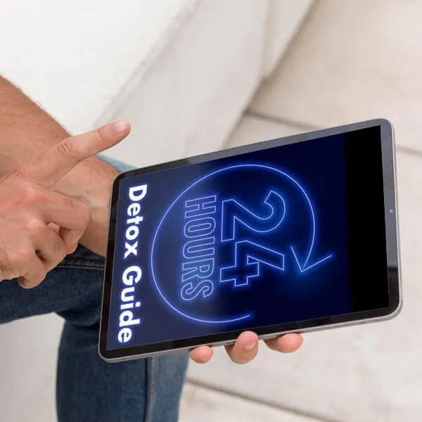 A hand holding a tablet that shows the e-book cover 24 Hours Detox Guide